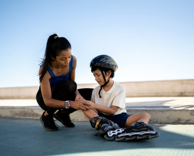 mom comforting son in rollerblades, clutching his leg