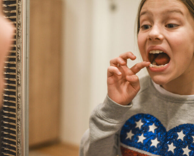 girl feeling her loose tooth and looking in the mirror