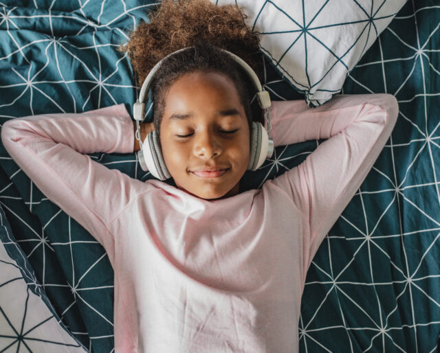Young girl laying in bed enjoying music, she is listening to music via wireless headphones