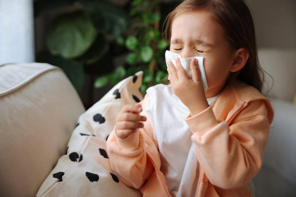 Sick little schoolgirl coughs and blows nose wiping with white paper napkin.