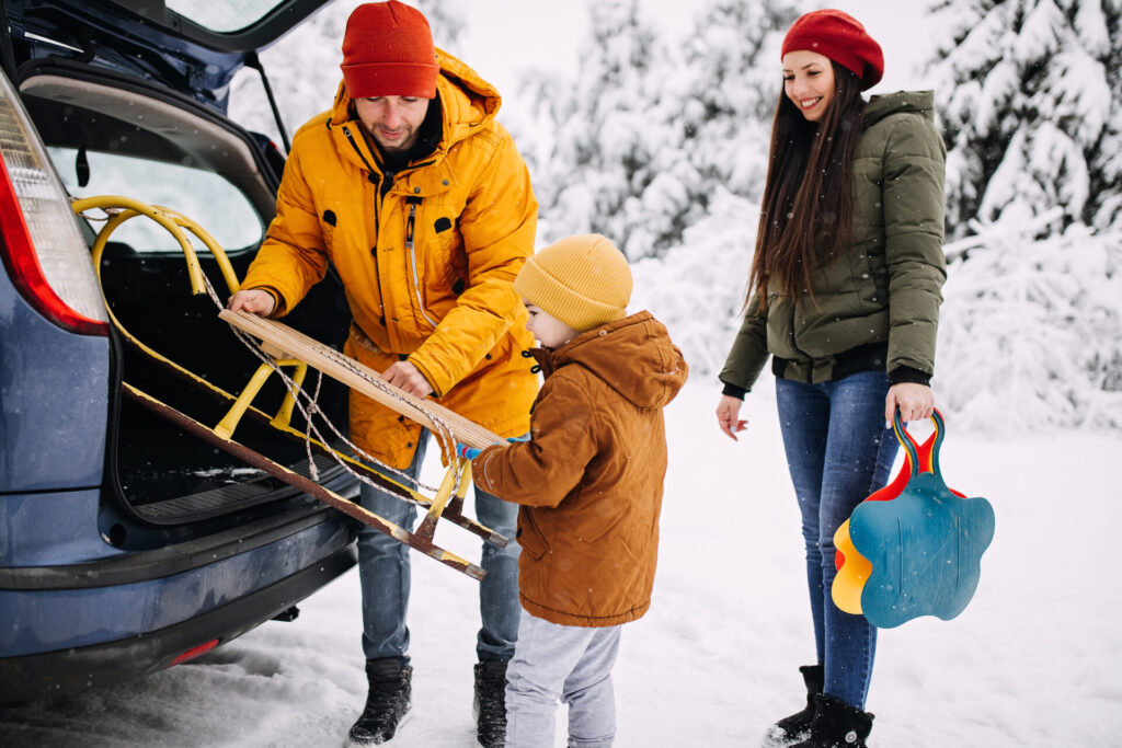 Family loading a sled into the back of a car in snowy weather