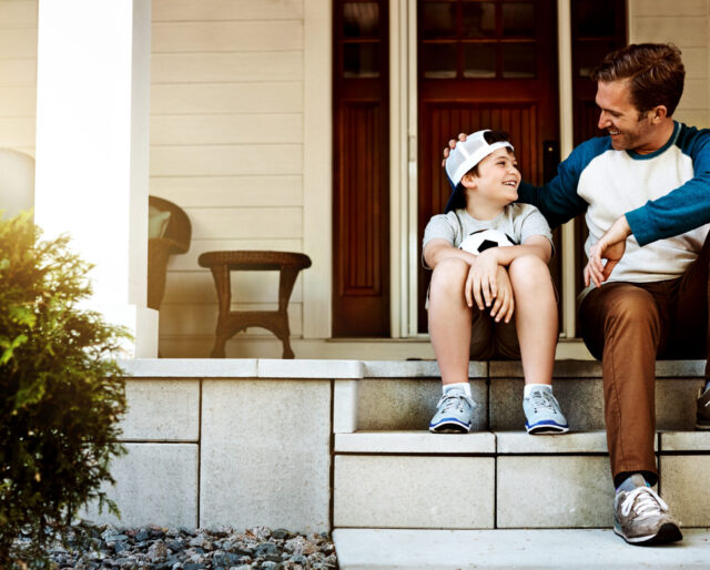 young boy and father sitting on a porch, talking and smiling