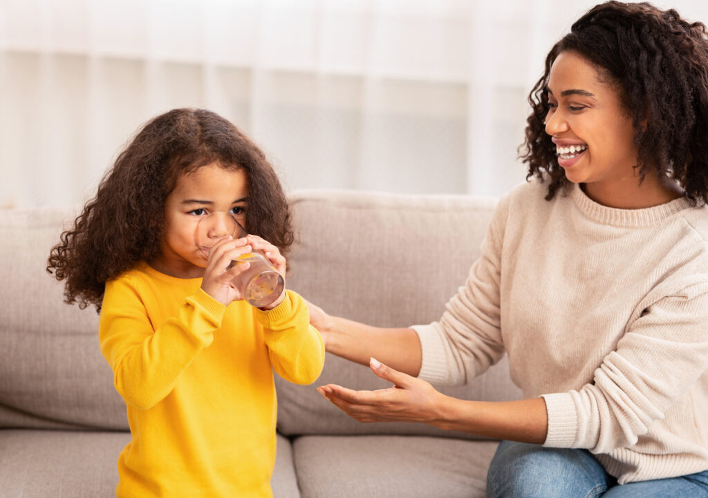 mom giving young daughter a glass of water and helping her drink it