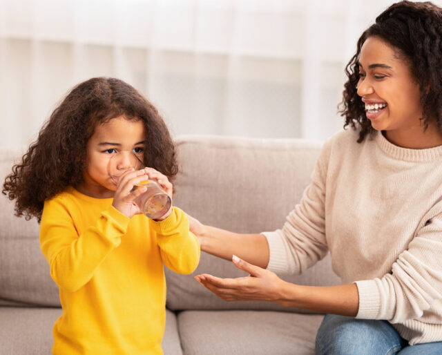 mom giving young daughter a glass of water and helping her drink it