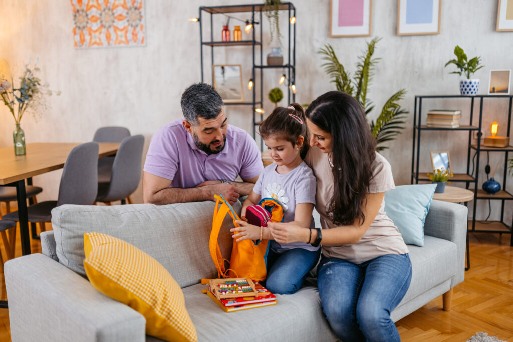 Young mother and father preparing their daughter for school. Packing a backpack together.