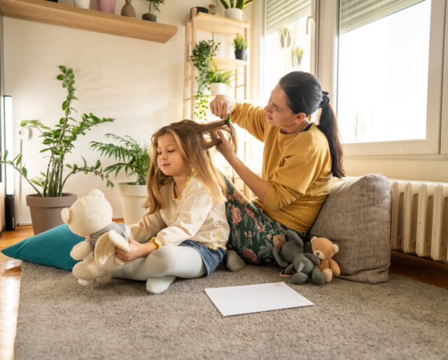 Getty images. Full length shot of mother doing head lice cleaning on little daughter while sitting on floor at home